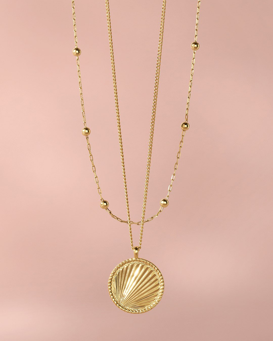 two gold necklaces on pink background