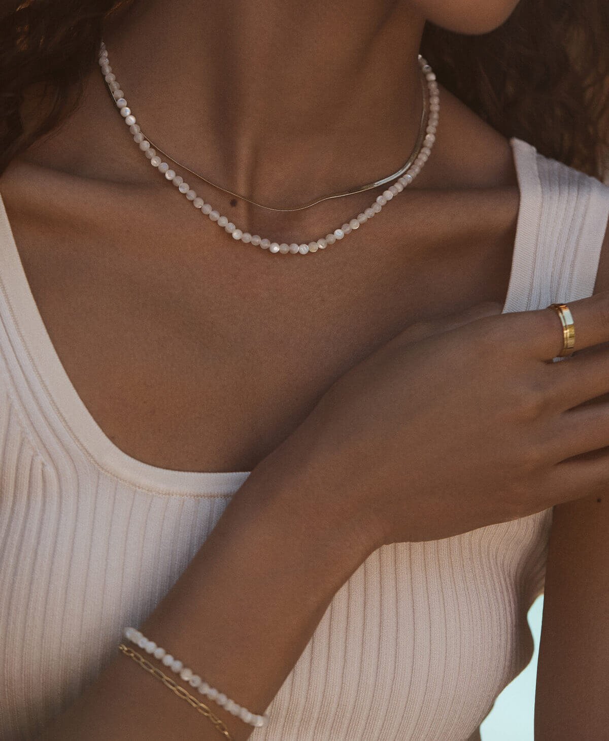 close up of woman wearing gemstone bracelets and necklaces and gold plated jewelry. 