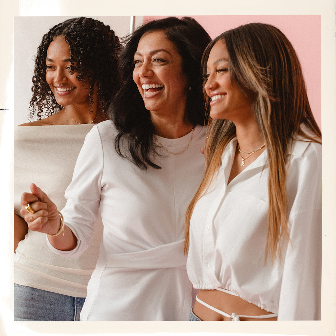 Three women sitting together, smiling and laughing against a pink background