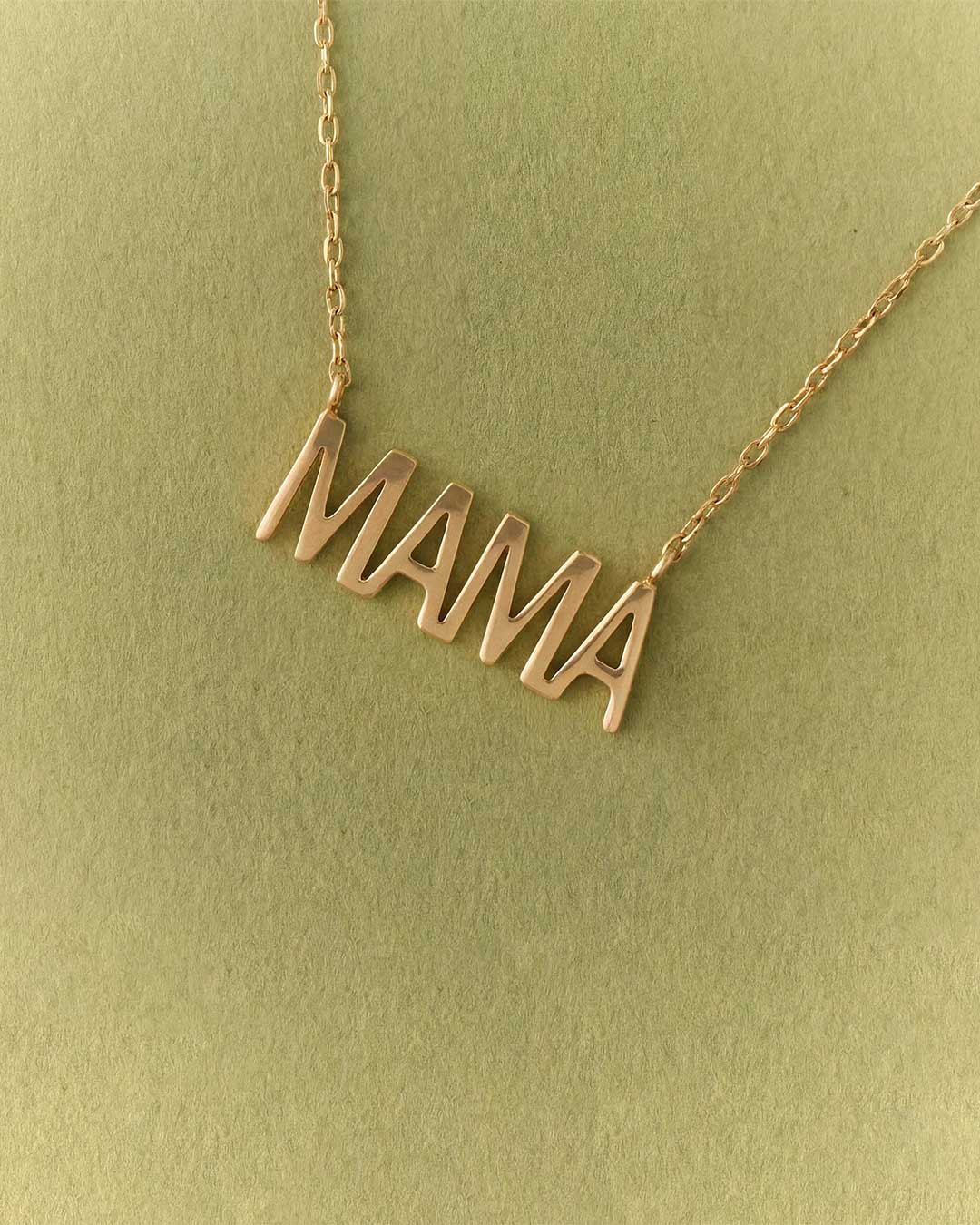 Gold 'MAMA' necklace on a green background