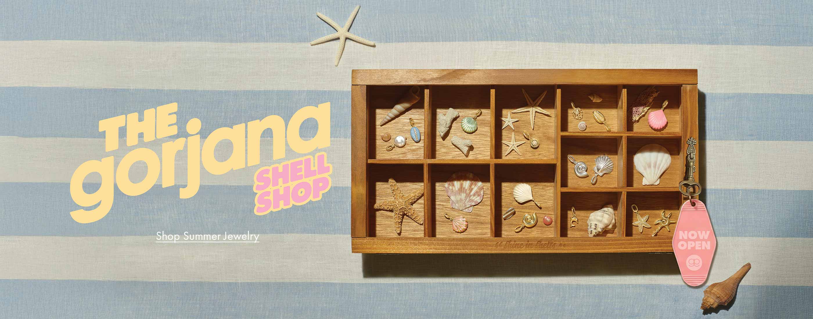 Wooden jewelry box with shell jewelry on a striped background, featuring 'The Gorjana Shell Shop' branding.