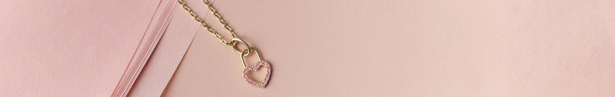 Pink background and a pink diamond heart charm. Shop the Pink Collection