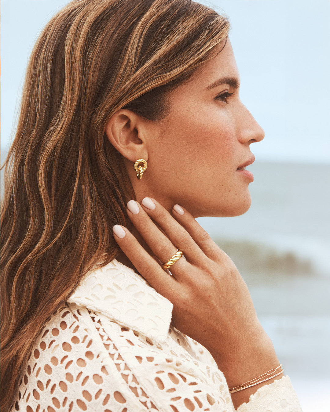 Woman wearing gold twisted hoops and a ring.