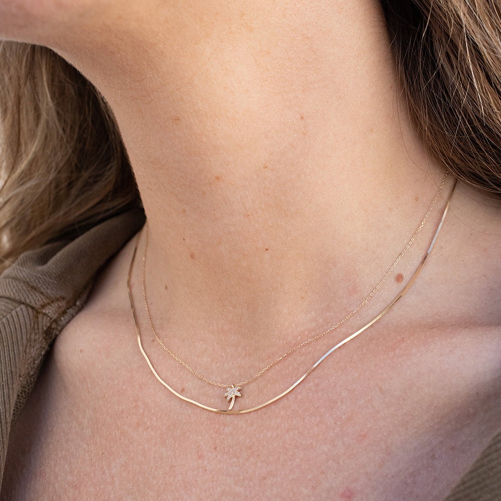 Woman wearing 14k gold necklaces, a herringbone chain and diamond palm tree necklace.