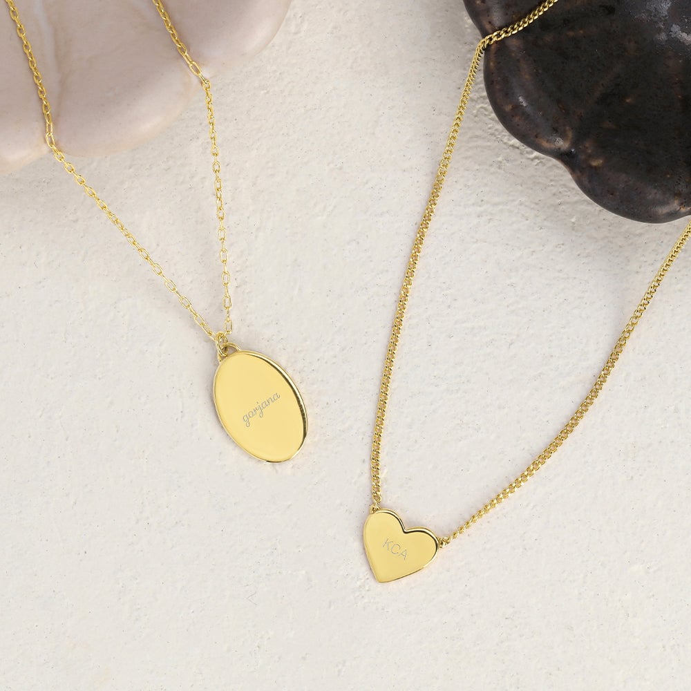 Gold oval necklaces with Gorjana engraved on it and a Gold heart necklace with the initials KCA engraved on it