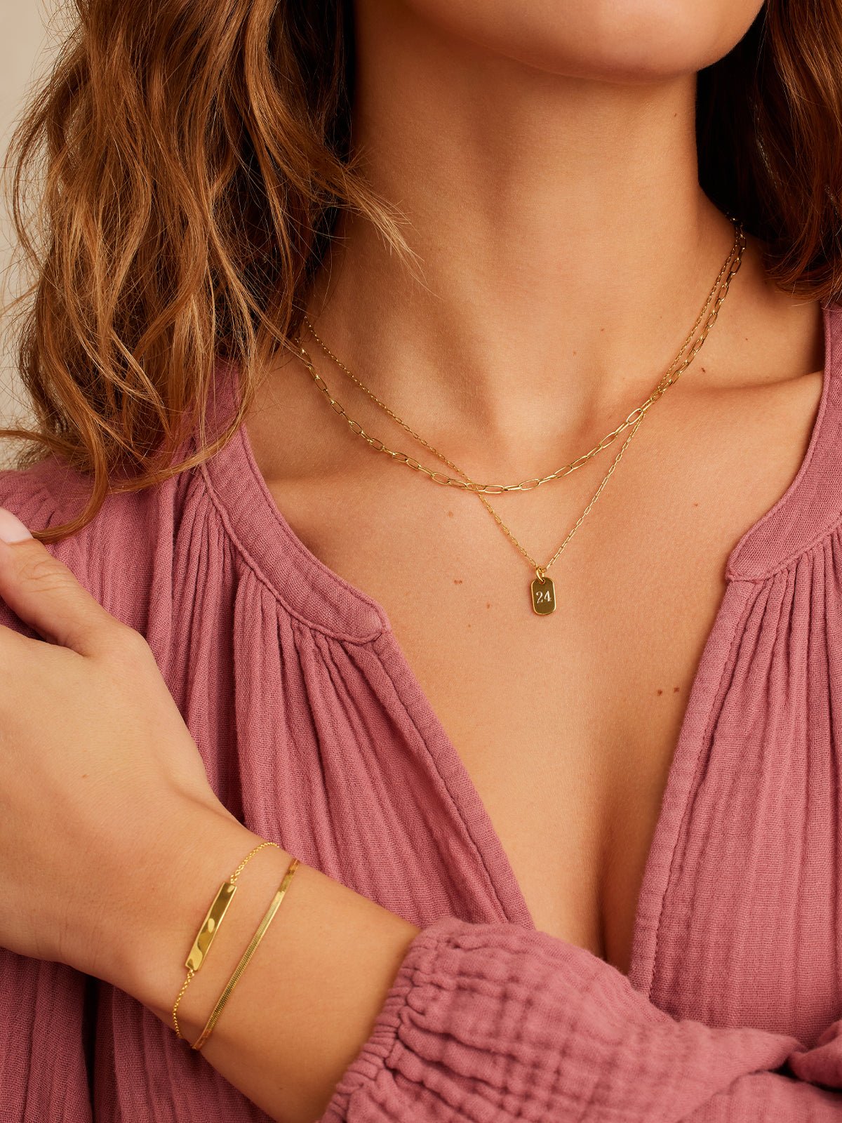 woman in a mauve long sleeve shirt with gold necklace set and gold bracelet set
