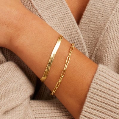 A woman in a cream sweater with a set of two gold bracelets adorning her wrist