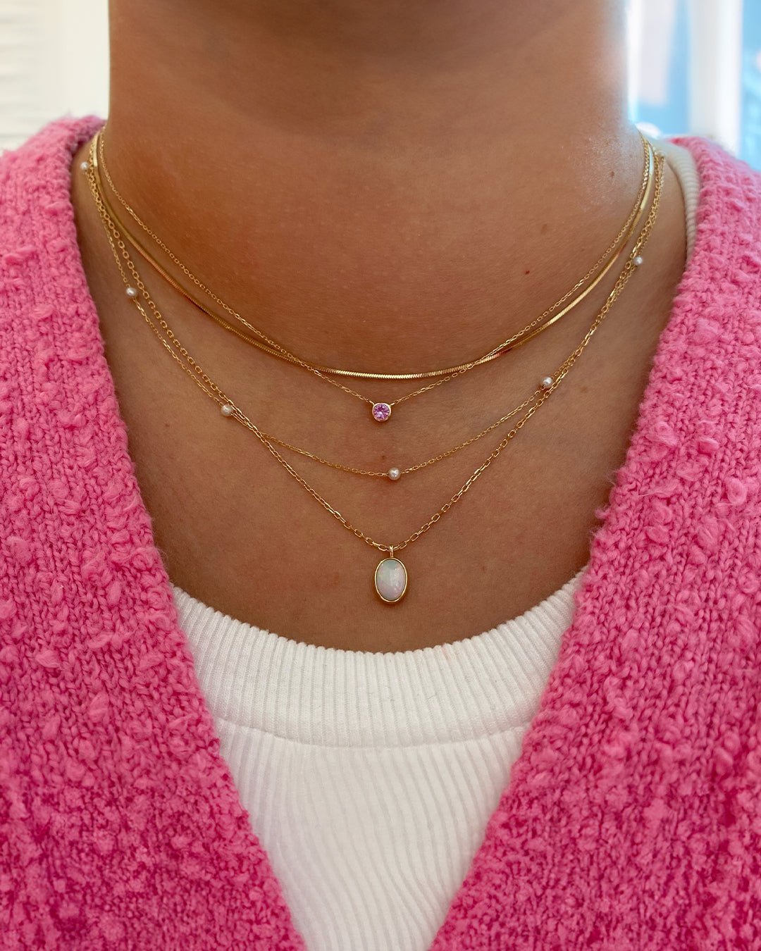 Woman wearing 14k gold necklaces with the pink sapphire BCRF necklace. 