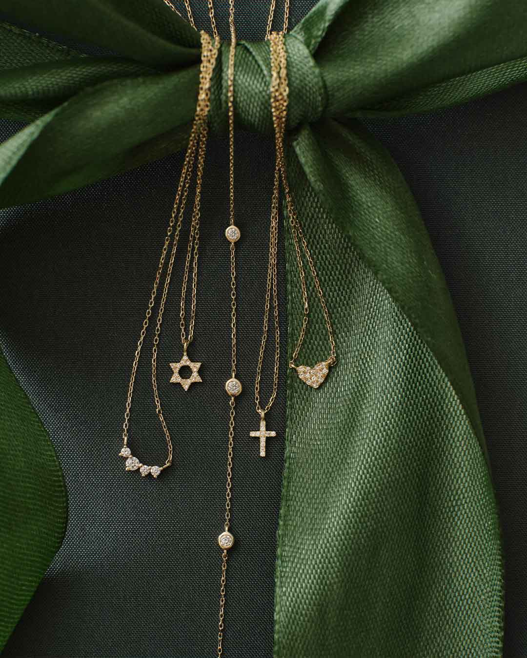 Gold necklaces with various pendants on a green fabric background