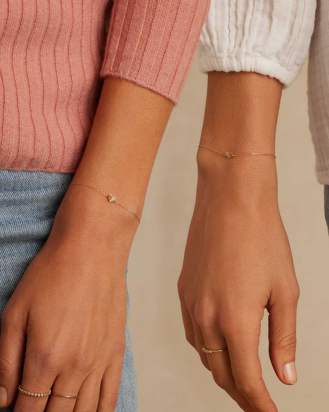 Two women wearing matching diamond heart bracelets. 