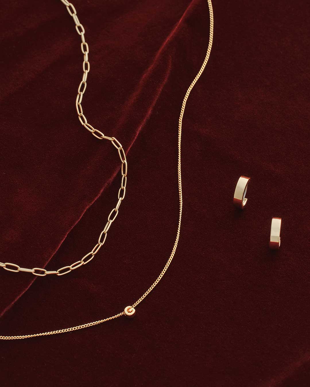 Gold chain necklace and earrings on a burgundy velvet background