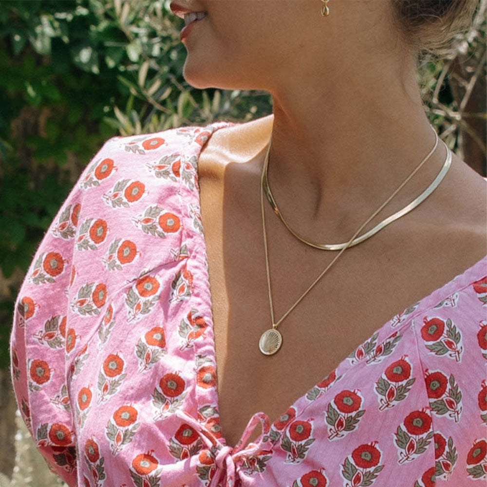 woman in pink summery dress with gold necklaces
