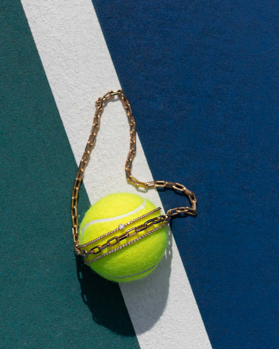 Yellow tennis ball with gold chain on a blue and white striped background