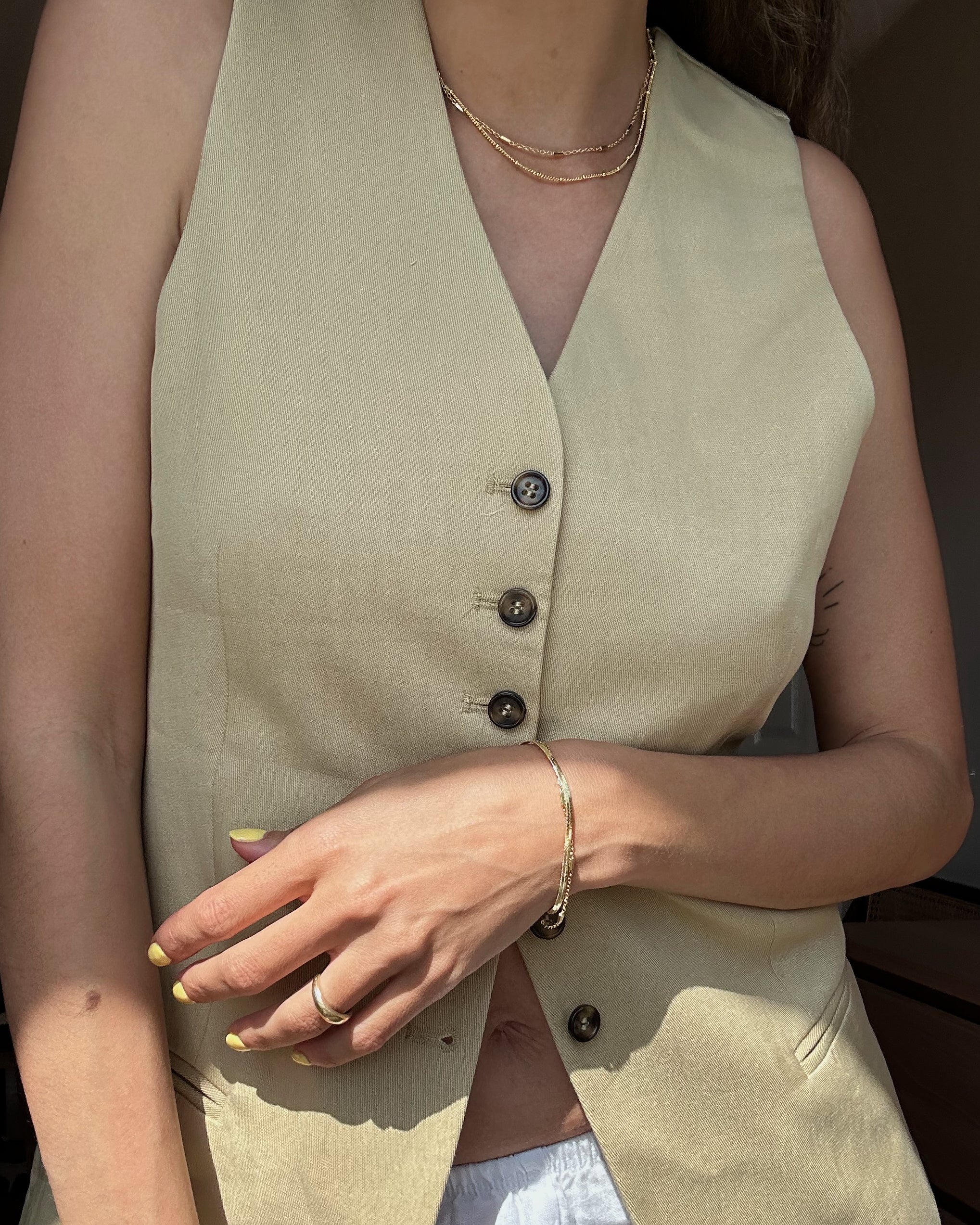 woman in vest blazer with gold bracelets and gold necklaces
