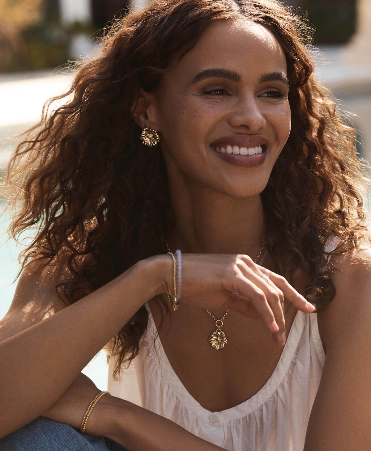 Woman smiling wearing gold plated floral and gemstone jewelry. 
