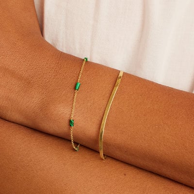 tanned wrist with two gold bracelets