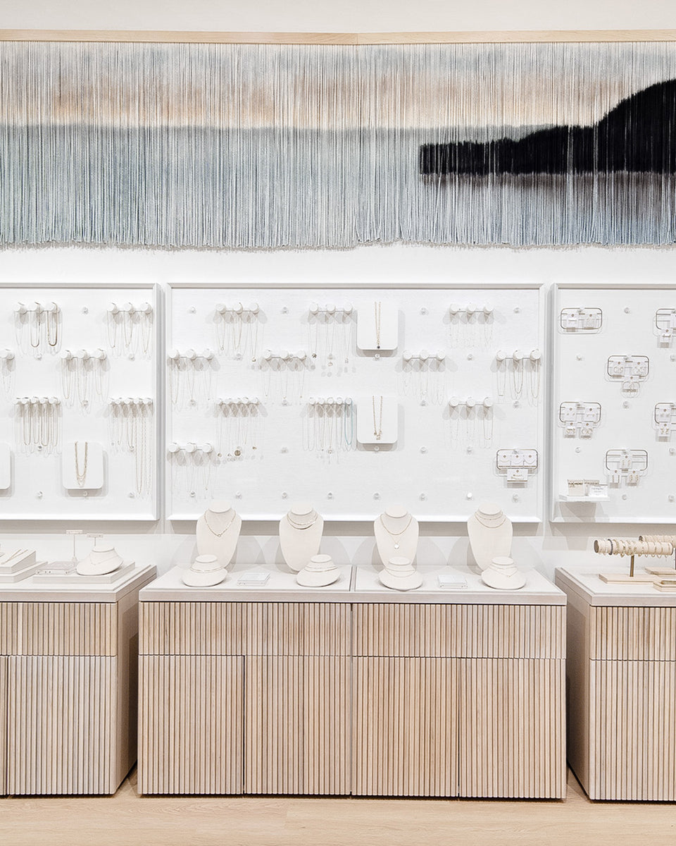 White wall with shelves of jewelry and jewelry stands on cases below 