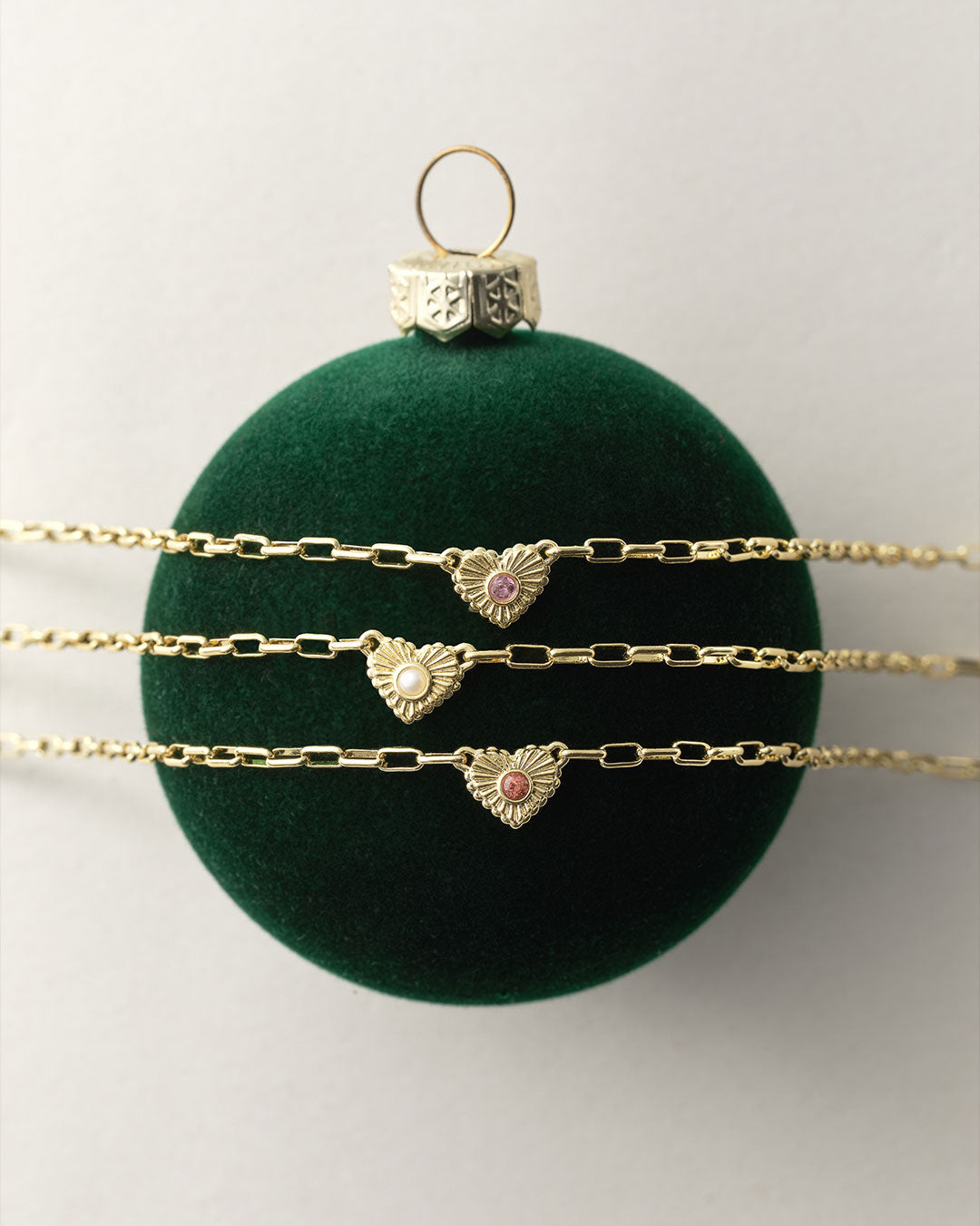 Gold heart-shaped necklaces on a green velvet ball against a white background
