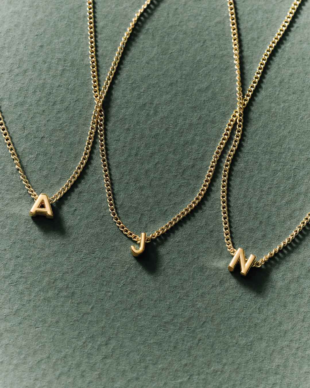 Three gold necklaces with letter pendants on a green surface