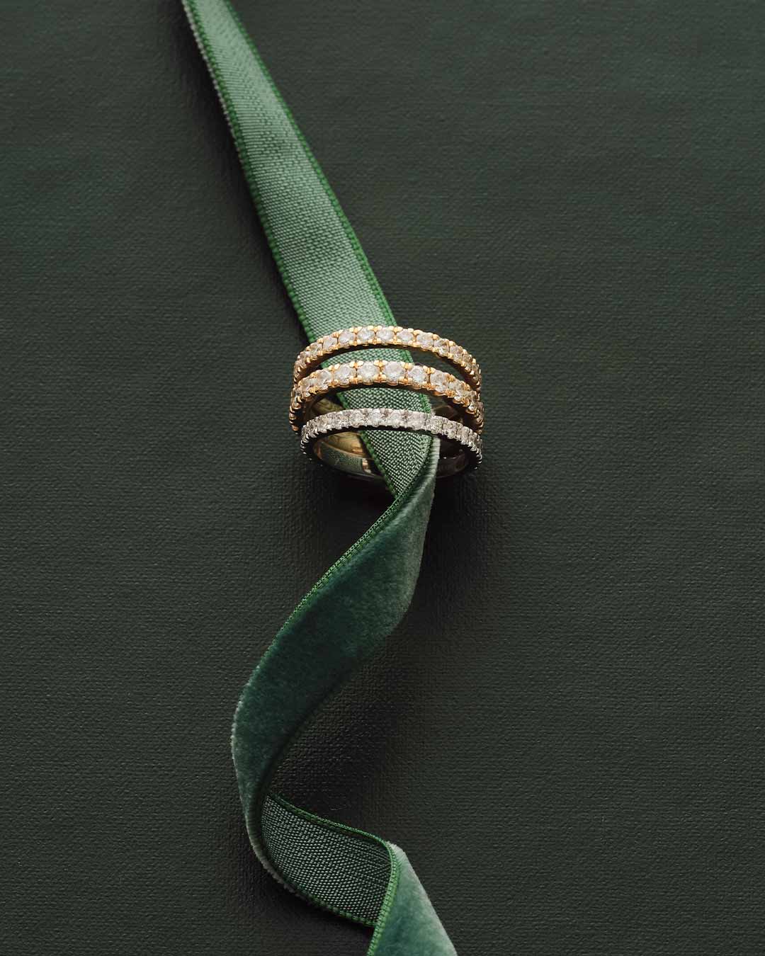 Three diamond rings stacked on a green ribbon against a dark green background