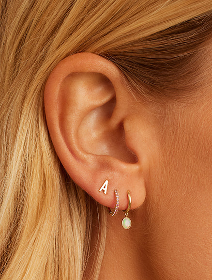 Woman wearing 14k gold huggies and studs. Shop Earrings. 