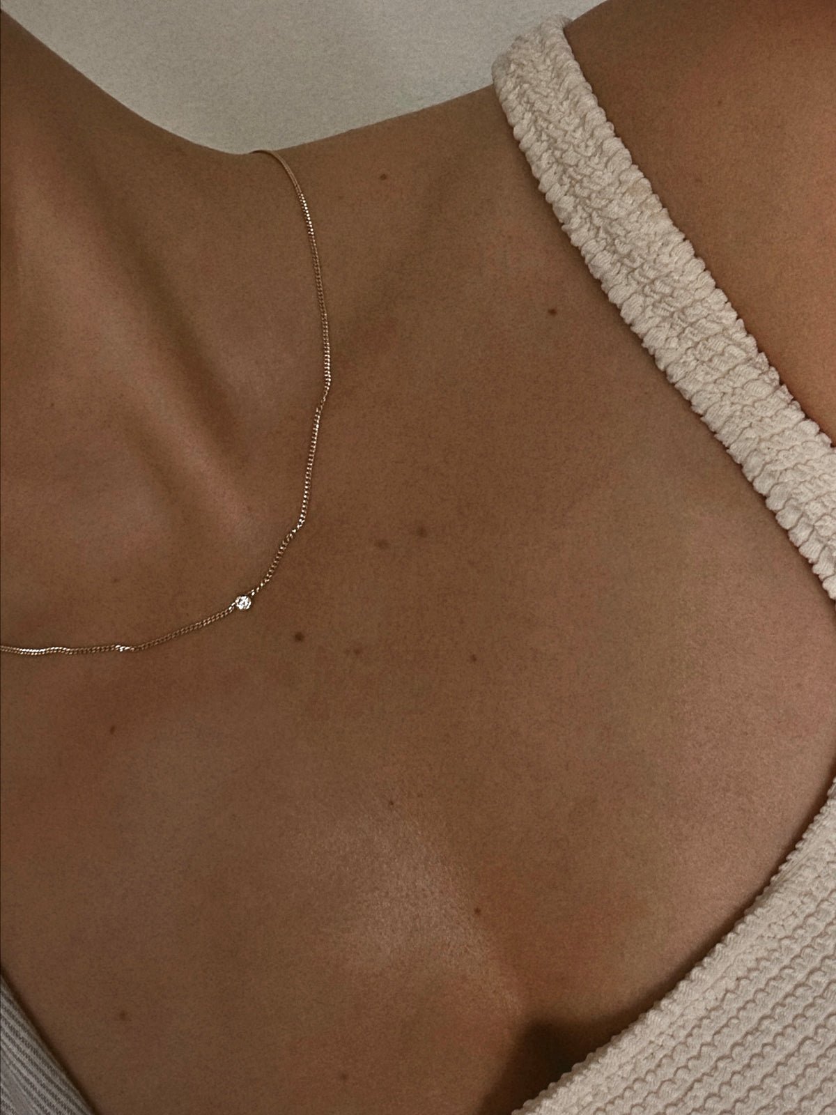 Woman wearing 14k gold chain necklace with diamond in center. 