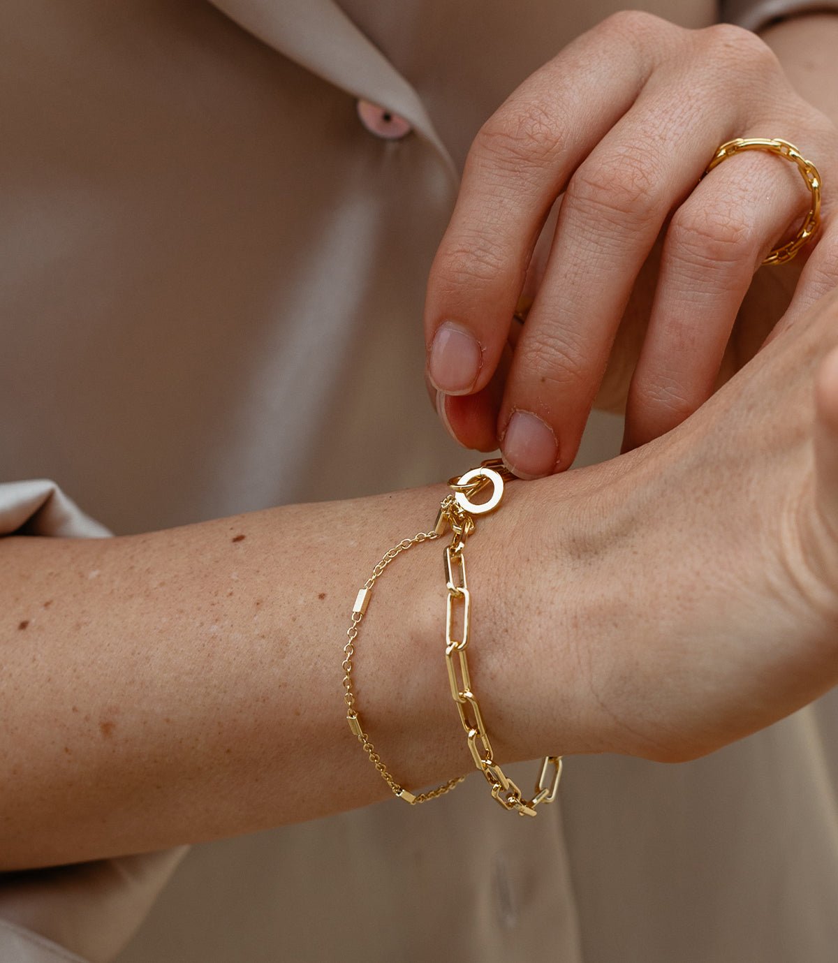 Woman wearing gold plated bracelets and a chain link ring 
