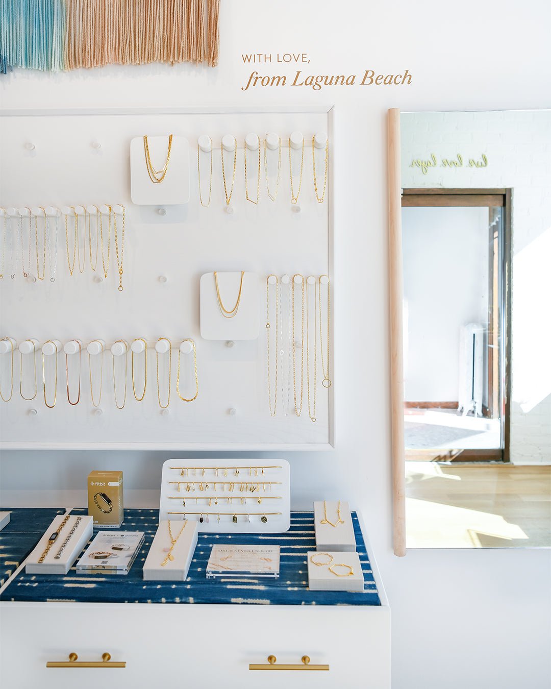 necklaces hanging on white wall with jewelry table filled with rings