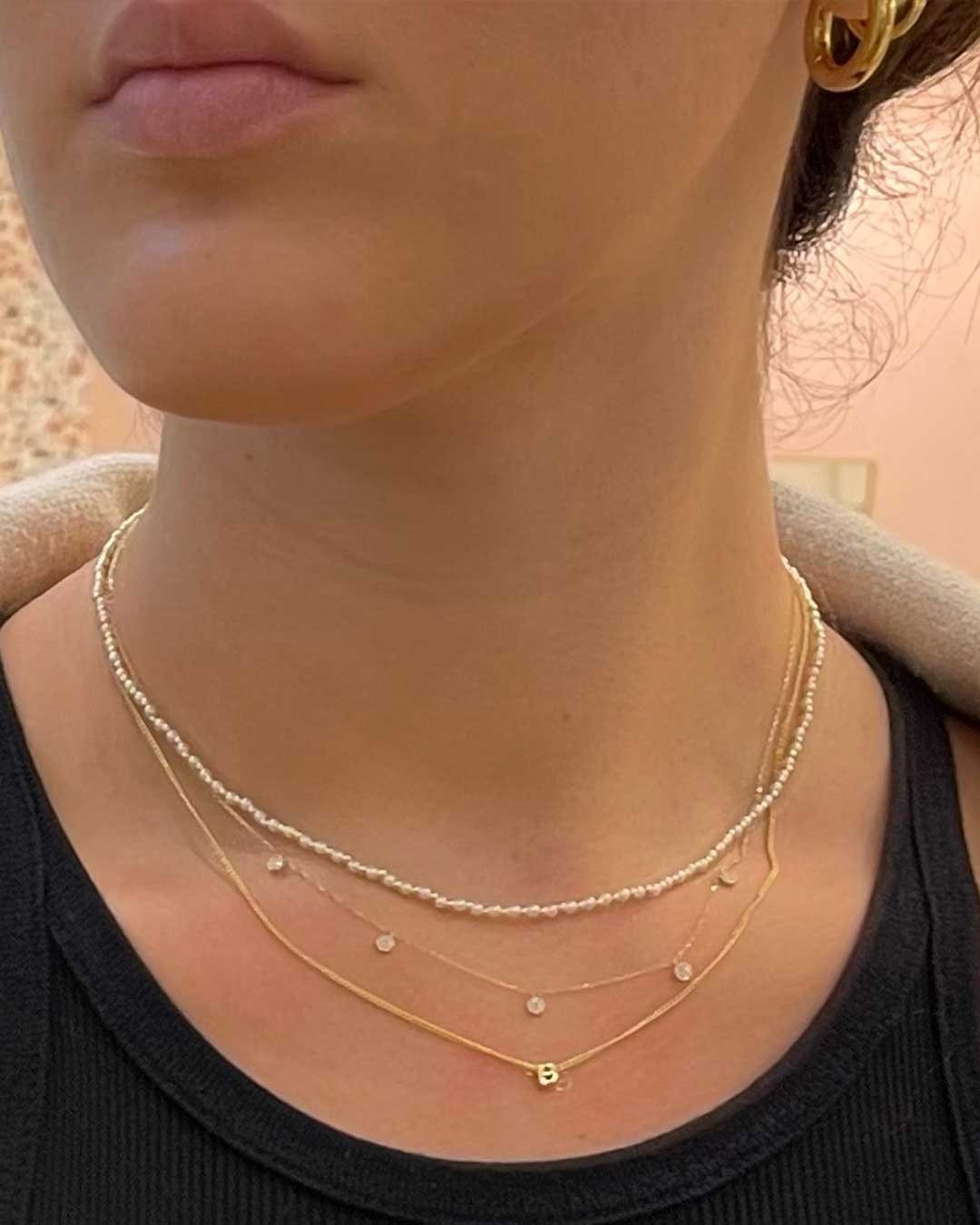 Woman wearing pearl, initial and diamond necklaces. 