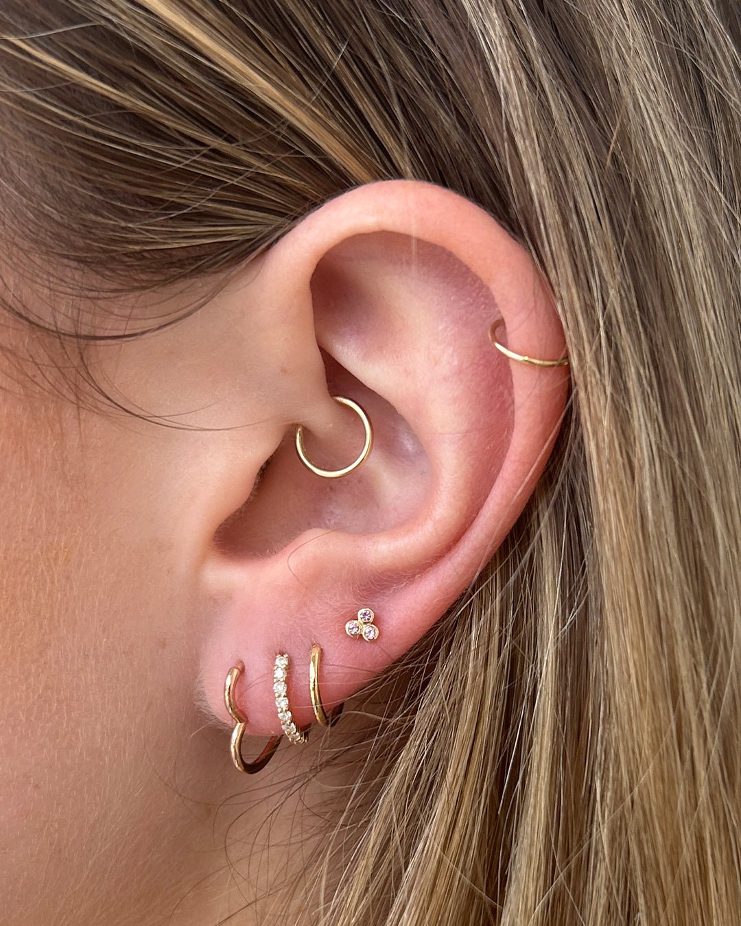 Woman wearing 14k gold and diamond earrings with a 14k rose gold heart huggie. 