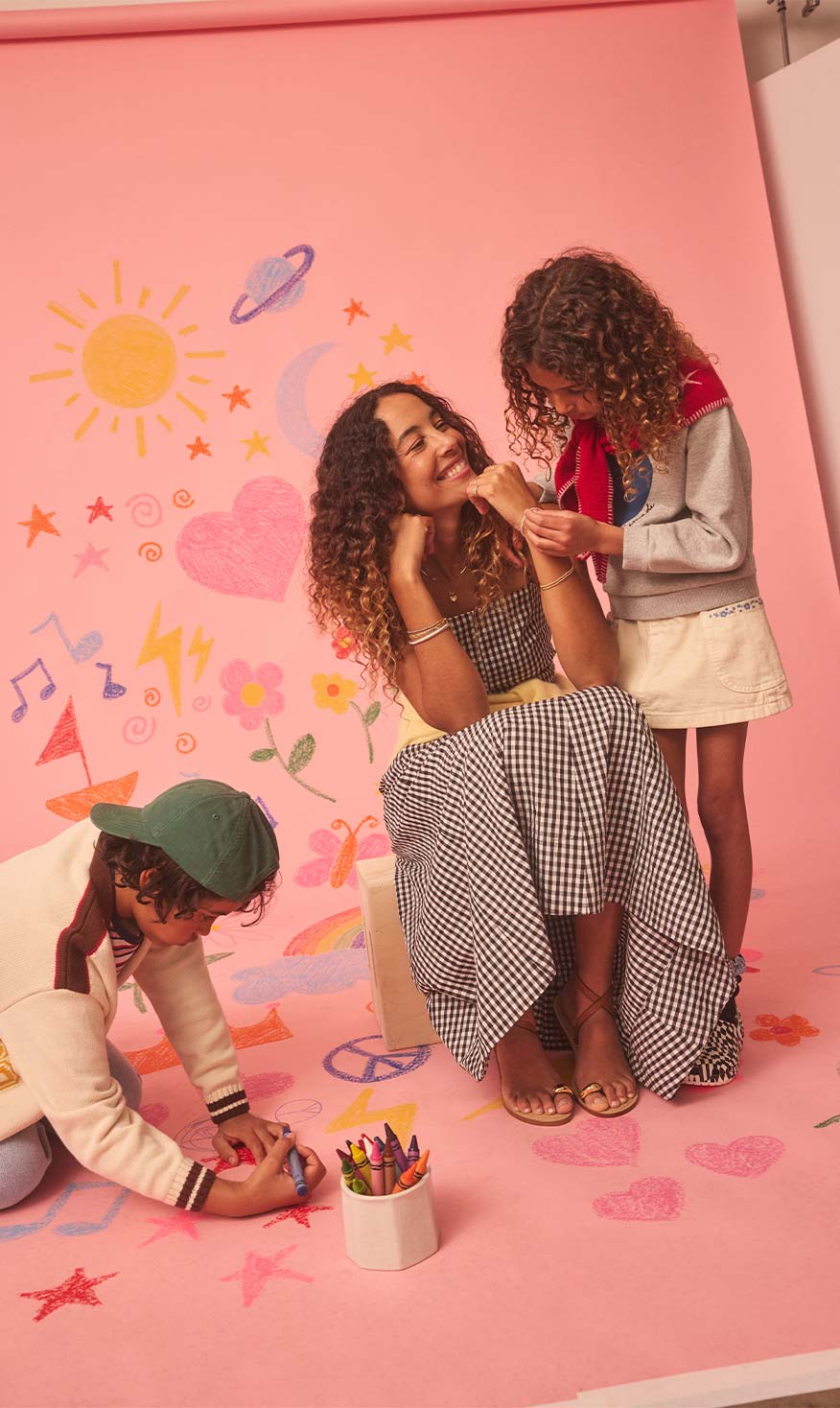 Paloma sitting on a chair with hertwo children in front of a pink wall with colorful decorations.